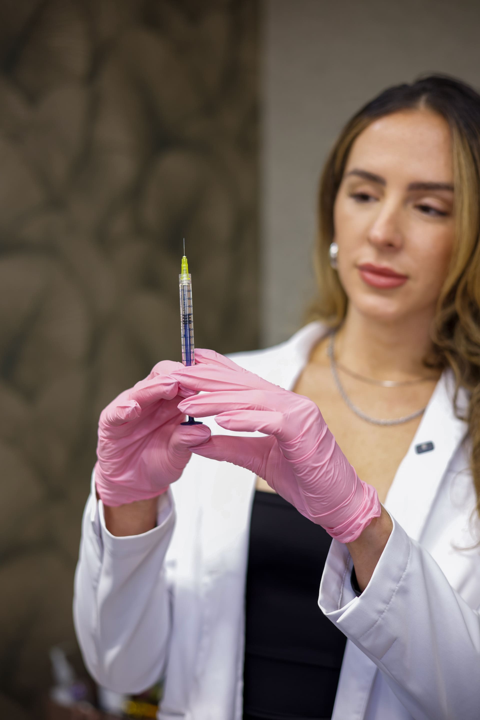 Profesional de estética con guantes rosas sosteniendo una jeringa.
